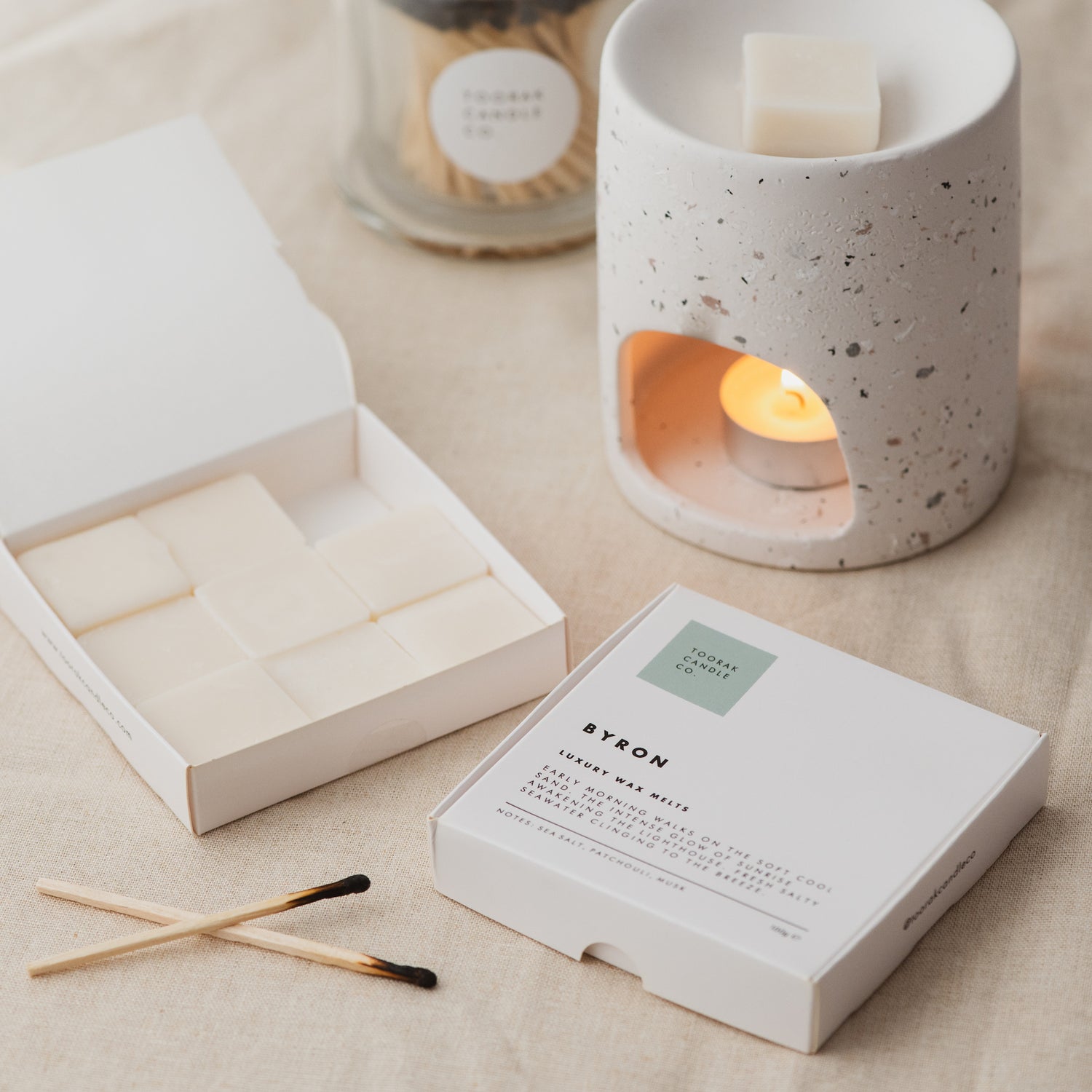 BYRON wax melts with ceramic wax melt burner, open box of wax melts and matches on a cream linen background