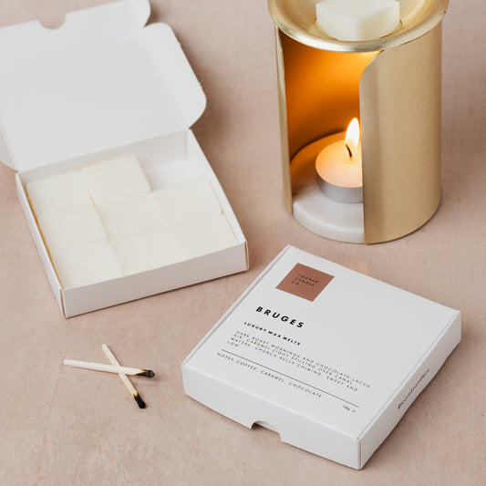 Wax melt luxury packaging with matches and a lit candle in the background on a beige surface