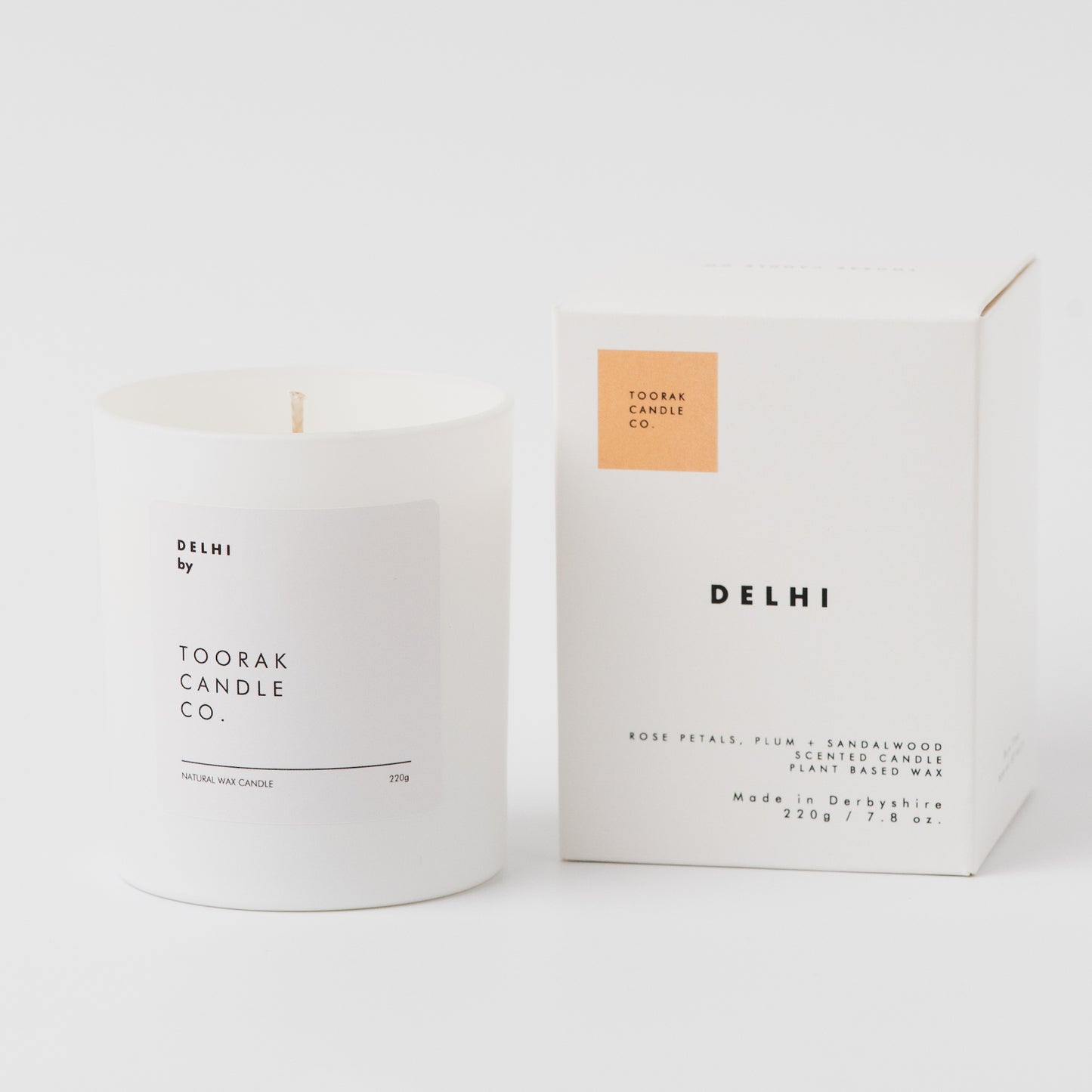 White candle with 'Delhi' branding next to its packaging on a white background