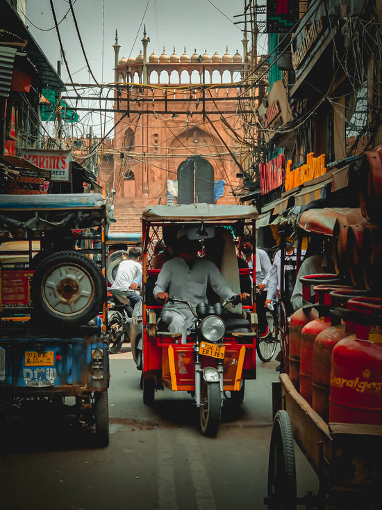 Man riding a rickshaw through a bustling street in Delhi, India
