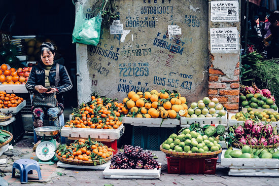 Woman sitting at a vibrant fruit stall on a street in Hanoi, Vietnam