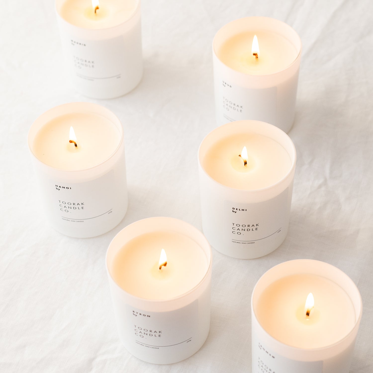 six lit white eco-friendly candles against a white crinkled background