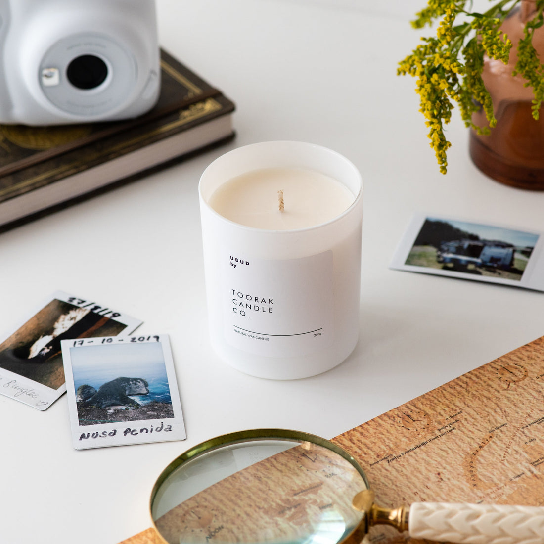 UBUD candle with camera, map, printed polaroids of travelling, plant and magnifying glass