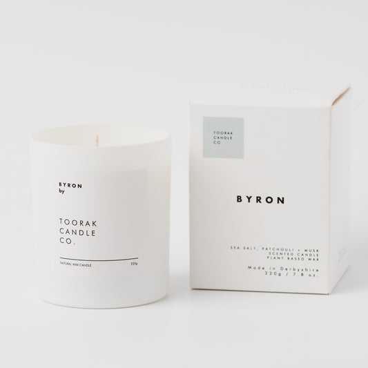 White candle with 'BYRON' branding next to its packaging on a white background