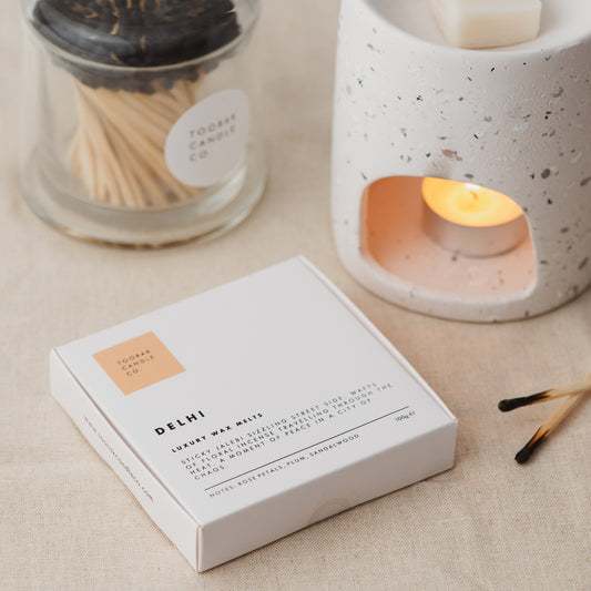 DELHI wax melts with lit candle in wax melt burner, and branded grey-tipped matches 