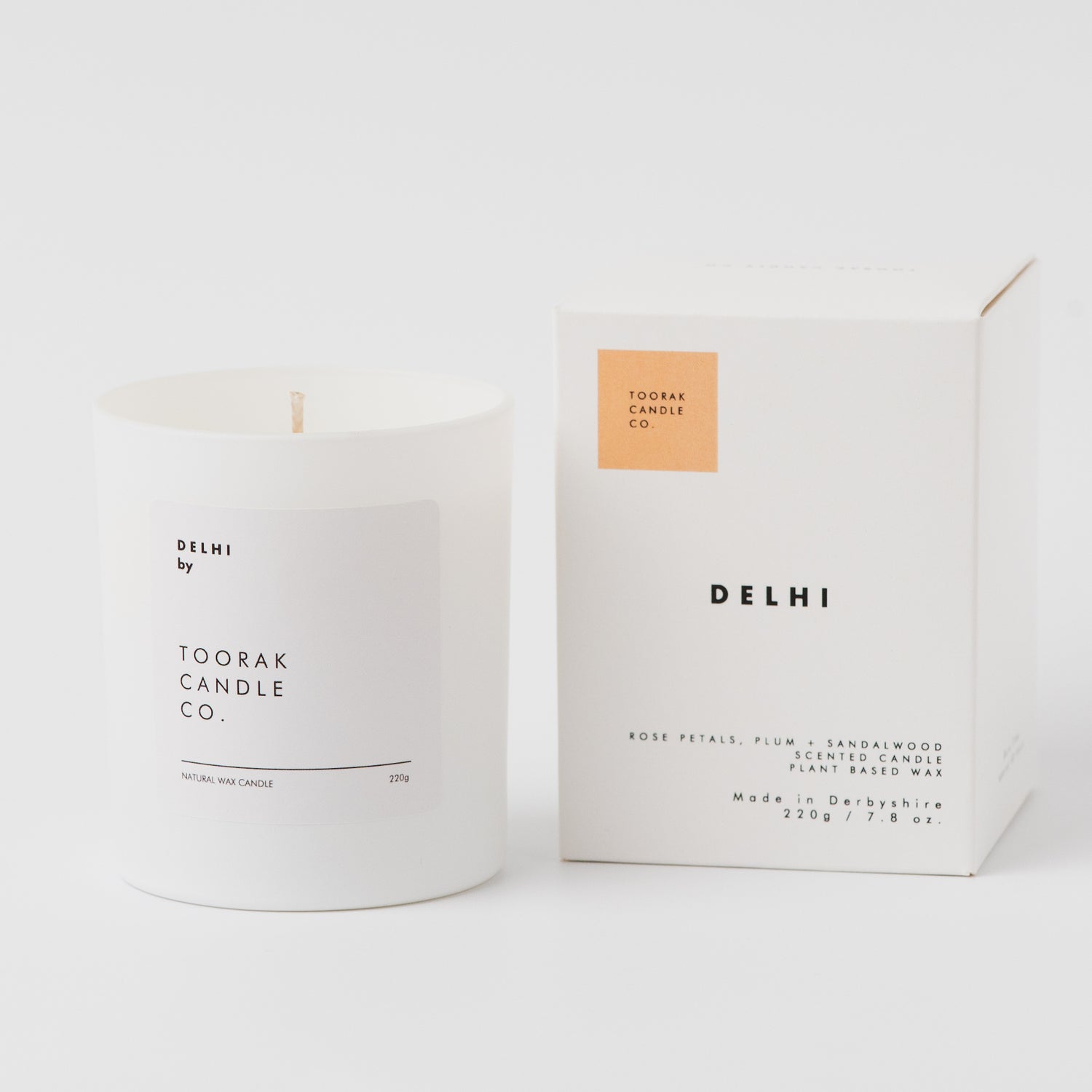 White candle with 'Delhi' branding next to its packaging on a white background