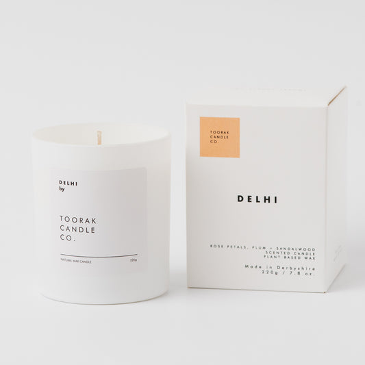 White candle with 'Delhi' branding next to its packaging on a white background