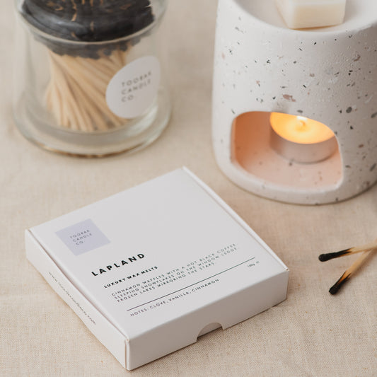 LAPLAND wax melts on a cream linen background with a lit wax melt burner and branded matches 